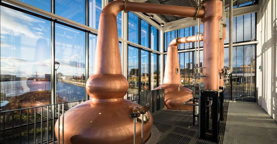 Copper pot stills behind glass at a city distillery